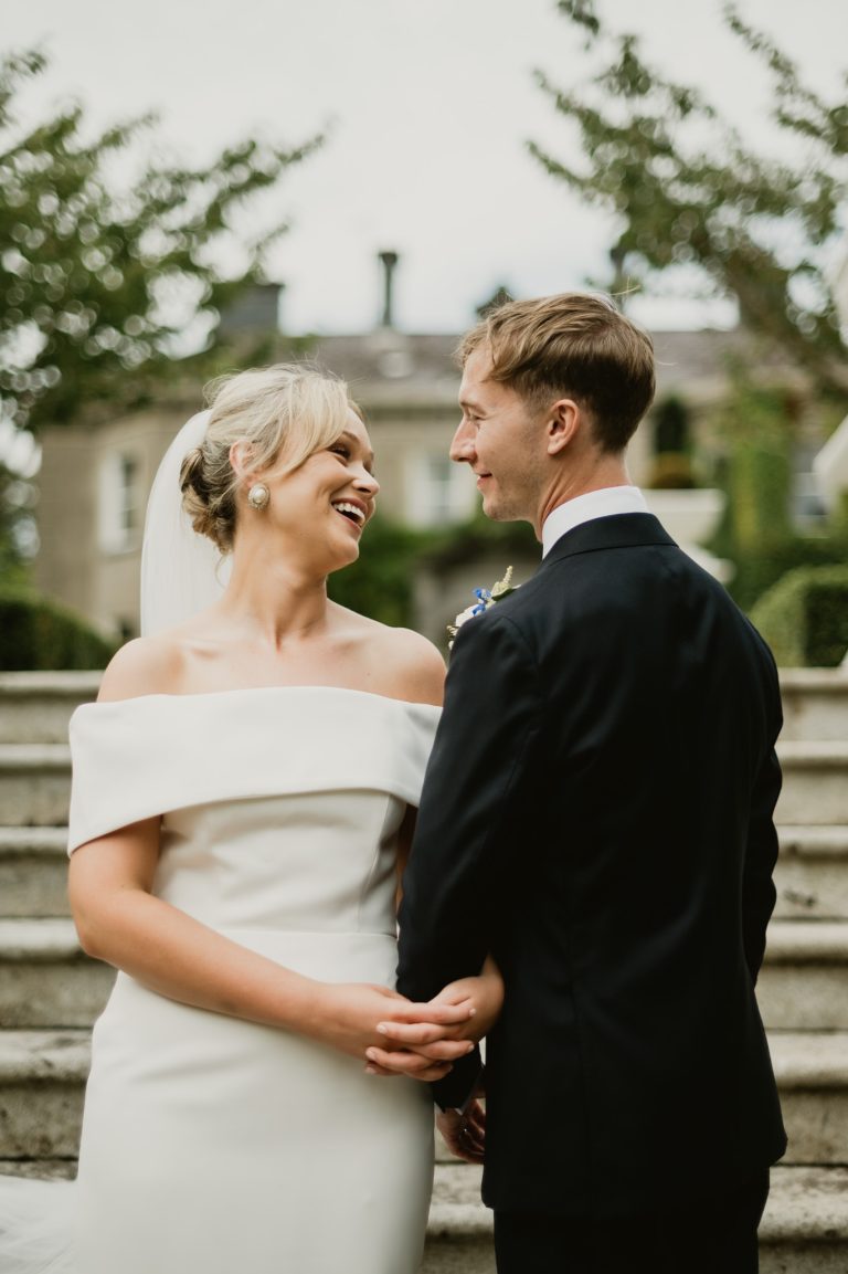 Romantic and intimate moment of the bride and groom sharing a kiss on the famous staircase at Tinakilly Country House in Ireland. This fine art wedding photograph beautifully captures love, connection, and elegance, highlighting the couple’s chemistry and the grandeur of the historic location. Photographed by WeddingWithMe, this image showcases professional wedding photography and videography, ideal for Irish wedding galleries, social media, and SEO-optimized luxury wedding website content.